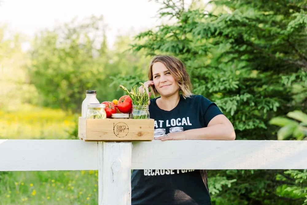 Bobbie Parr with a crate of Parr's Jars salts and fresh produce on a fence in Northwestern Ontario